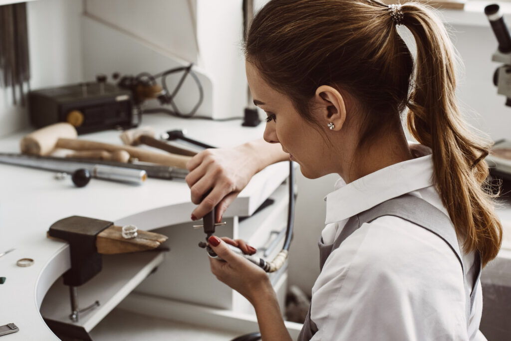 Seitenansicht einer Juwelierin, die in ihrer Schmuckwerkstatt die Werkzeuge für die Arbeit mit Silberringen vorbereitet