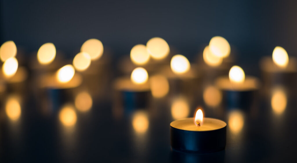 Flammen vieler Kerzen, die auf schwarzem Hintergrund brennen, als Symbol der Trauer