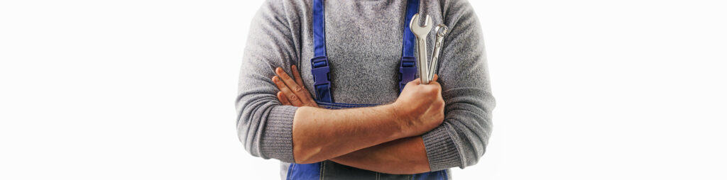 Hausmeister steht im Blaumann Overall mit Werkzeug in der Hand bereit.