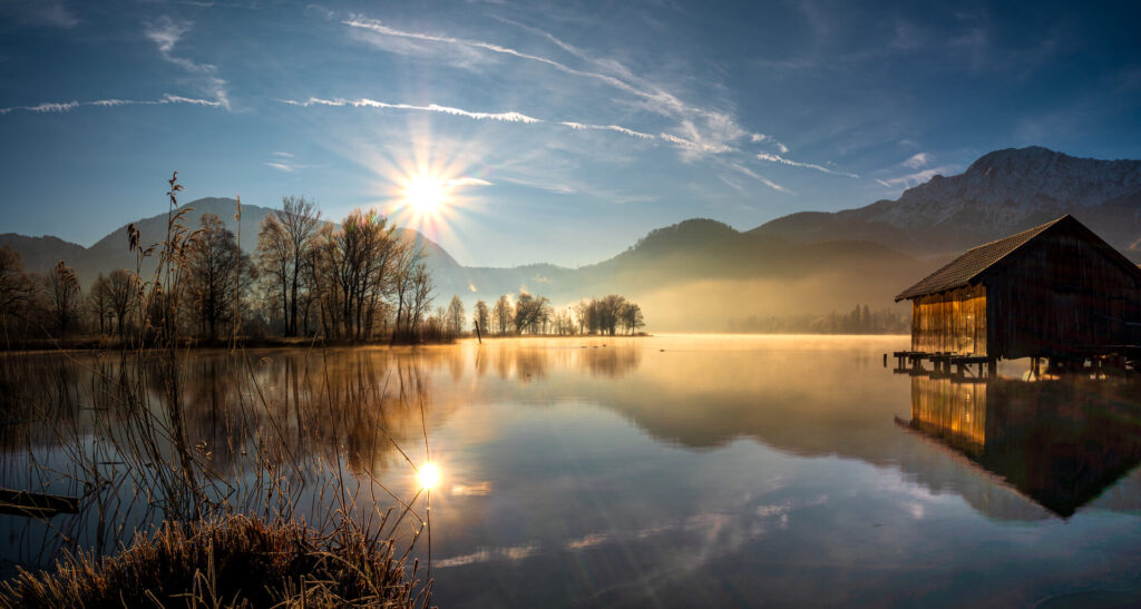 Idyllischer Morgensonnenblick auf den bayerischen Kochelsee mit angrenzendem Ferienhaus.