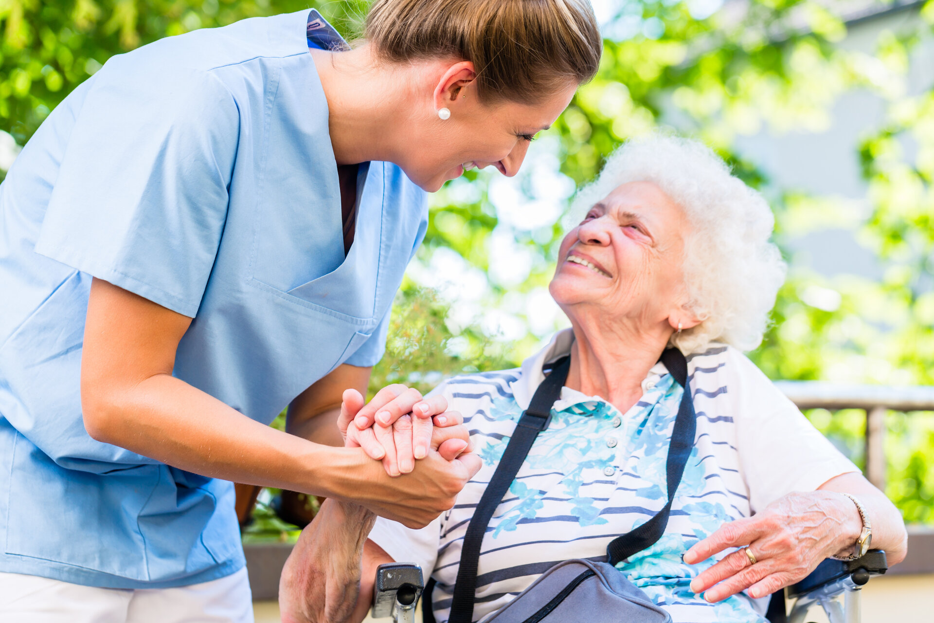 Altenpflegerin reicht Seniorin im Rollstuhl die Hand