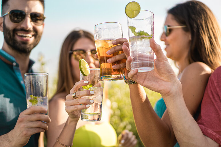 Eine Gruppe junger Leute stößt im Sommer im Freien mit Cocktailgläsern an. Versammlung von Freunden genießen Zeit zusammen im Freien